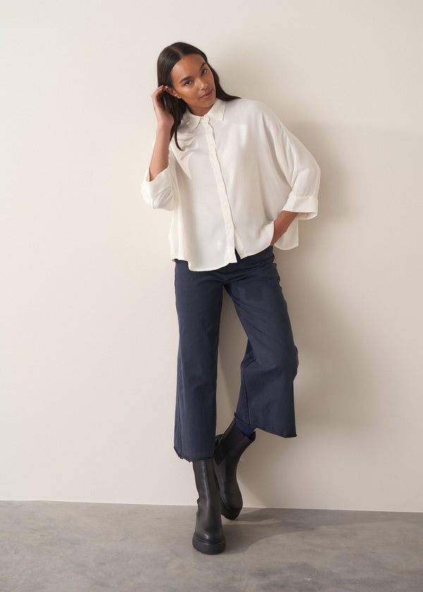 Woman wearing a white blouse and navy pants against a plain background