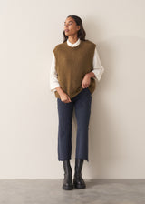 Woman wearing a white blouse and navy pants against a plain background