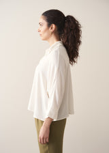 Woman wearing a creamy white blouse and green tapered trousers against a plain background