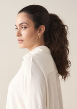 Woman wearing a creamy white blouse and green tapered trousers against a plain background