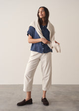 Woman wearing cropped tapered leg cord trousers in oatmeal  with blue linen shirt