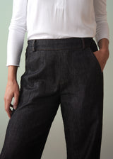 Person wearing dark cotton jeans with a tucked in white shirt against a plain background