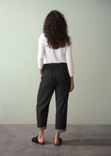 Person wearing a white top and dark cotton jeans against a plain background