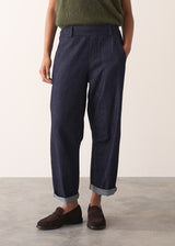 Woman wearing a green sleeveless sweater and dark blue jeans against a plain background