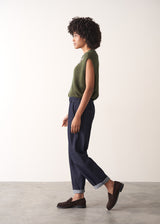 Woman wearing a green sleeveless sweater and dark blue jeans against a plain background