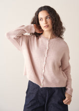 Woman wearing light blush pink button up cardigan with blue jeans
