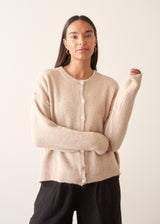 A woman wearing a light beigh knitted cardigan with a white t-shirt and black trousers.