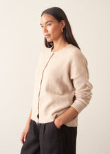 A woman wearing a light beigh knitted cardigan with a white t-shirt and black trousers.
