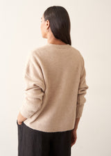A woman wearing a light beigh knitted cardigan with a white t-shirt and black trousers.