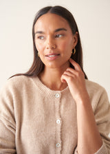 A woman wearing a light beigh knitted cardigan with a white t-shirt and black trousers.