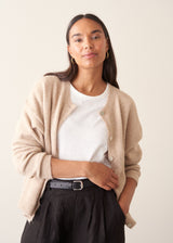 A woman wearing a light beigh knitted cardigan with a white t-shirt and black trousers.