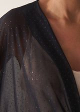 Close up of sheer sparkle draped top on model, styled with a cream camisole