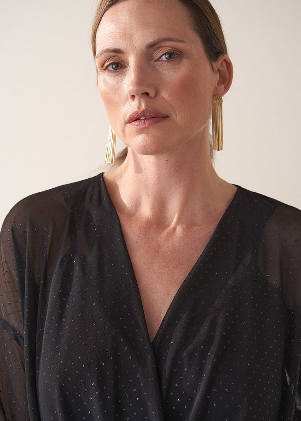 Woman wearing a black sheer top and black wide leg trousers against a plain background