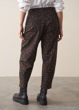 Woman wearing a white shirt and leopard print barrel leg jeans against a plain background