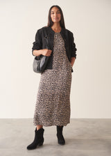 Woman wearing sleeveless satin leopard print dress with black boots and a black suede jacket