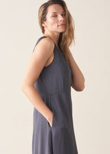 A woman wearing a sleeveless, maxi-length dark blue grey dress with a cocoon skirt