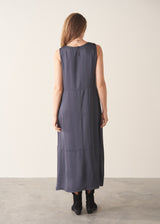 A woman wearing a sleeveless, maxi-length dark blue grey dress with a cocoon skirt