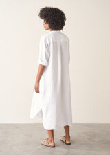 Woman wearing white linen shirt dress with button up detail and pleated from.