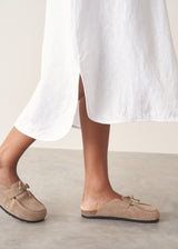 Woman wearing white linen shirt dress with button up detail and pleated from.