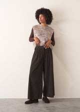 Woman wearing a sleeveless sweater and wide-leg brown corduroy trousers against a plain background