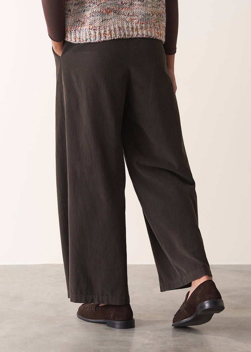 Woman wearing a sleeveless sweater and wide-leg brown corduroy trousers against a plain background