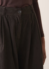 Woman wearing a sleeveless sweater and wide-leg brown corduroy trousers against a plain background