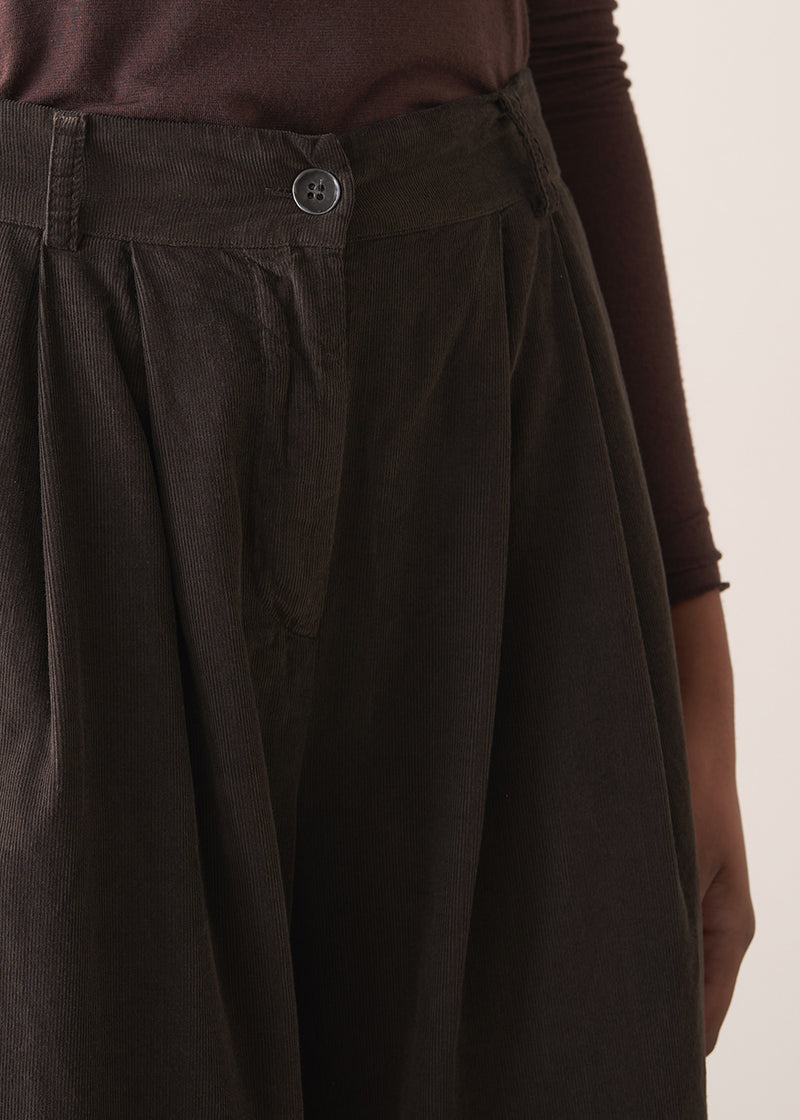 Woman wearing a sleeveless sweater and wide-leg brown corduroy trousers against a plain background