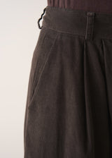 Woman wearing a sleeveless sweater and wide-leg brown corduroy trousers against a plain background