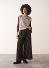 Woman wearing a sleeveless sweater and wide-leg brown corduroy trousers against a plain background