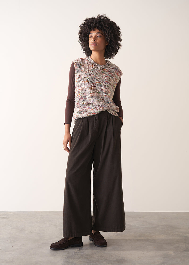 Woman wearing a sleeveless sweater and wide-leg brown corduroy trousers against a plain background