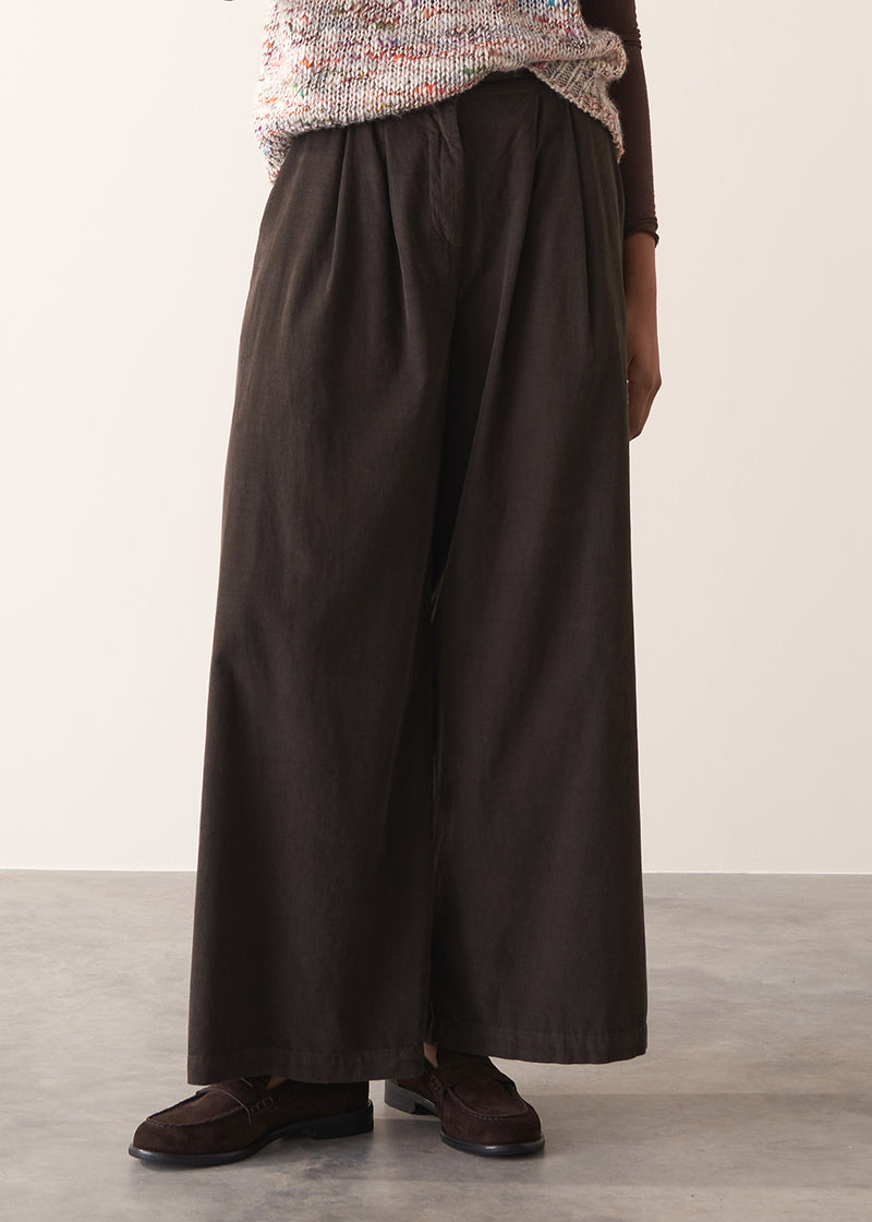 Woman wearing a sleeveless sweater and wide-leg brown corduroy trousers against a plain background