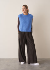 Woman wearing brown, wide leg corduroy trousers and a cornflower blue sleeveless sweater