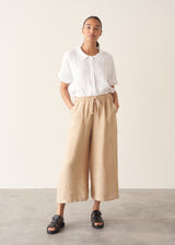 Woman wearing white linen shirt, sand wide leg linen trousers and black sandals