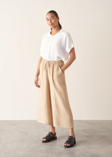 Woman wearing white linen shirt, sand wide leg linen trousers and black sandals