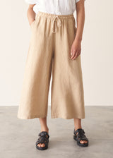 Woman wearing white linen shirt, sand wide leg linen trousers and black sandals