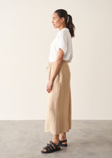Woman wearing white linen shirt, sand wide leg linen trousers and black sandals