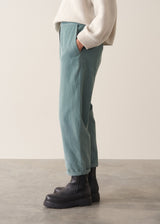 Woman wearing a cream rollneck sweater and aqua cord trousers against a plain background