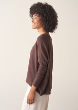 A woman wearing a chocolate brown, fine knit sweater and light cream trousers. 