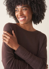 A woman wearing a chocolate brown, fine knit sweater and light cream trousers. 