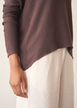 A woman wearing a chocolate brown, fine knit sweater and light cream trousers. 