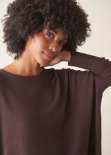 A woman wearing a chocolate brown, fine knit sweater and light cream trousers. 