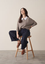 Woman wearing long sleeve stone-grey fine knit sweater with dark blue denim trousers