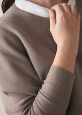 Woman wearing long sleeve stone-grey fine knit sweater with dark blue denim trousers