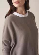 Woman wearing long sleeve stone-grey fine knit sweater with dark blue denim trousers