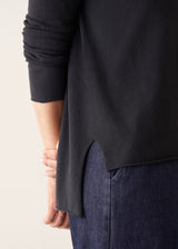 Woman wearing black lightweight knit sweater with blue jeans and a beige jacket
