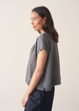 Woman wearing a blue and green check linen top and denim cullottes against a plain background