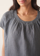 Woman wearing a blue and green check linen top and denim cullottes against a plain background