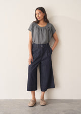 Woman wearing a blue and green check linen top and denim cullottes against a plain background