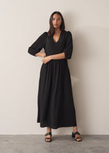 Woman wearing black full length maxi dress with puffed 3/4 length sleeves, with black leather sandals