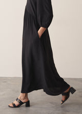 Woman wearing black full length maxi dress with puffed 3/4 length sleeves paired with black leather sandals